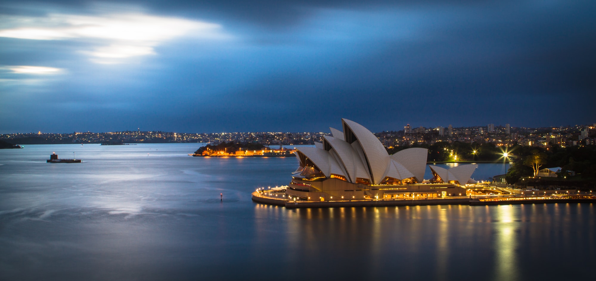 Sydney Opera House lit up across the harbour at dusk