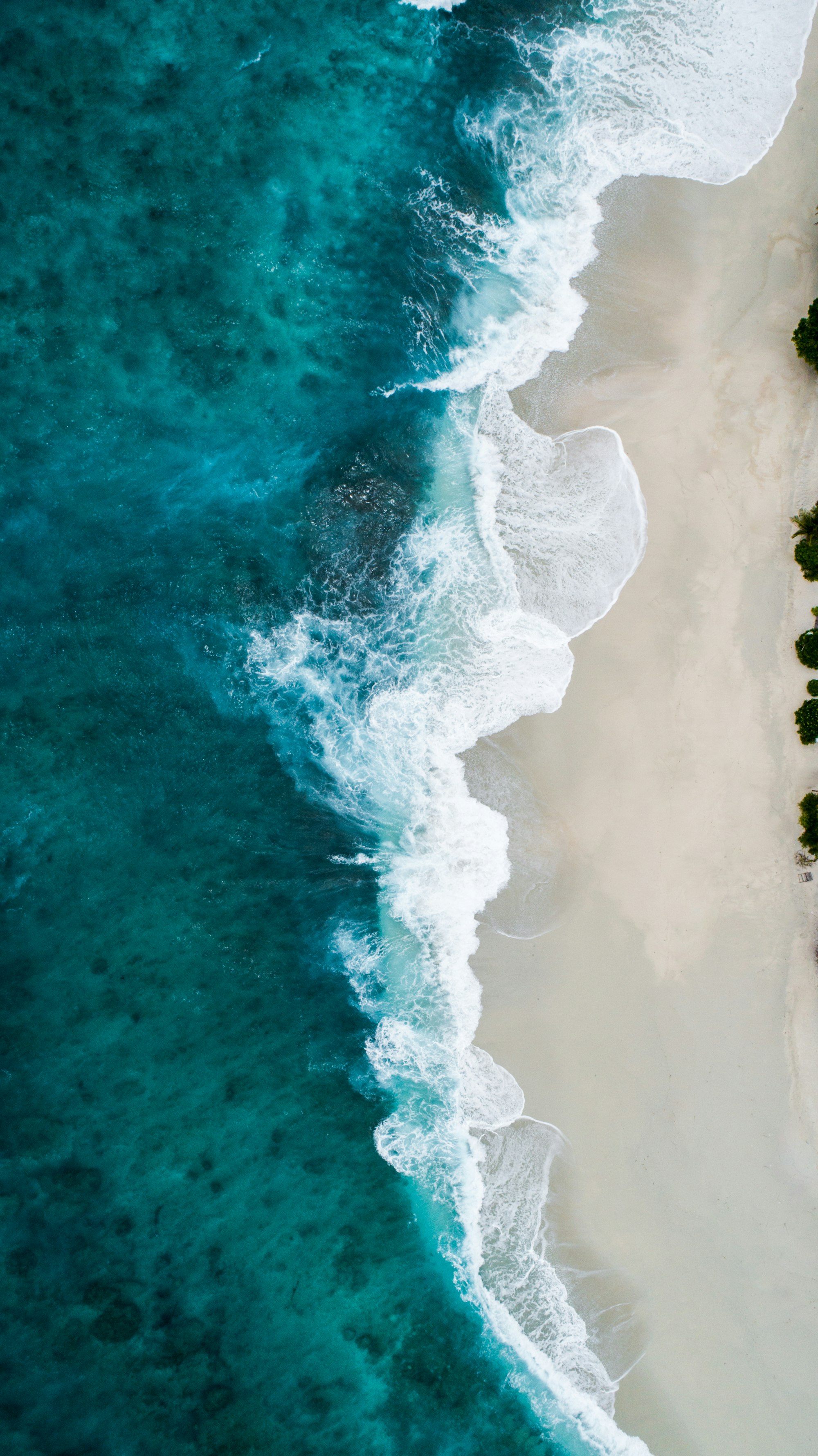 Aerial view of turquoise ocean waves breaking on a white-sand beach