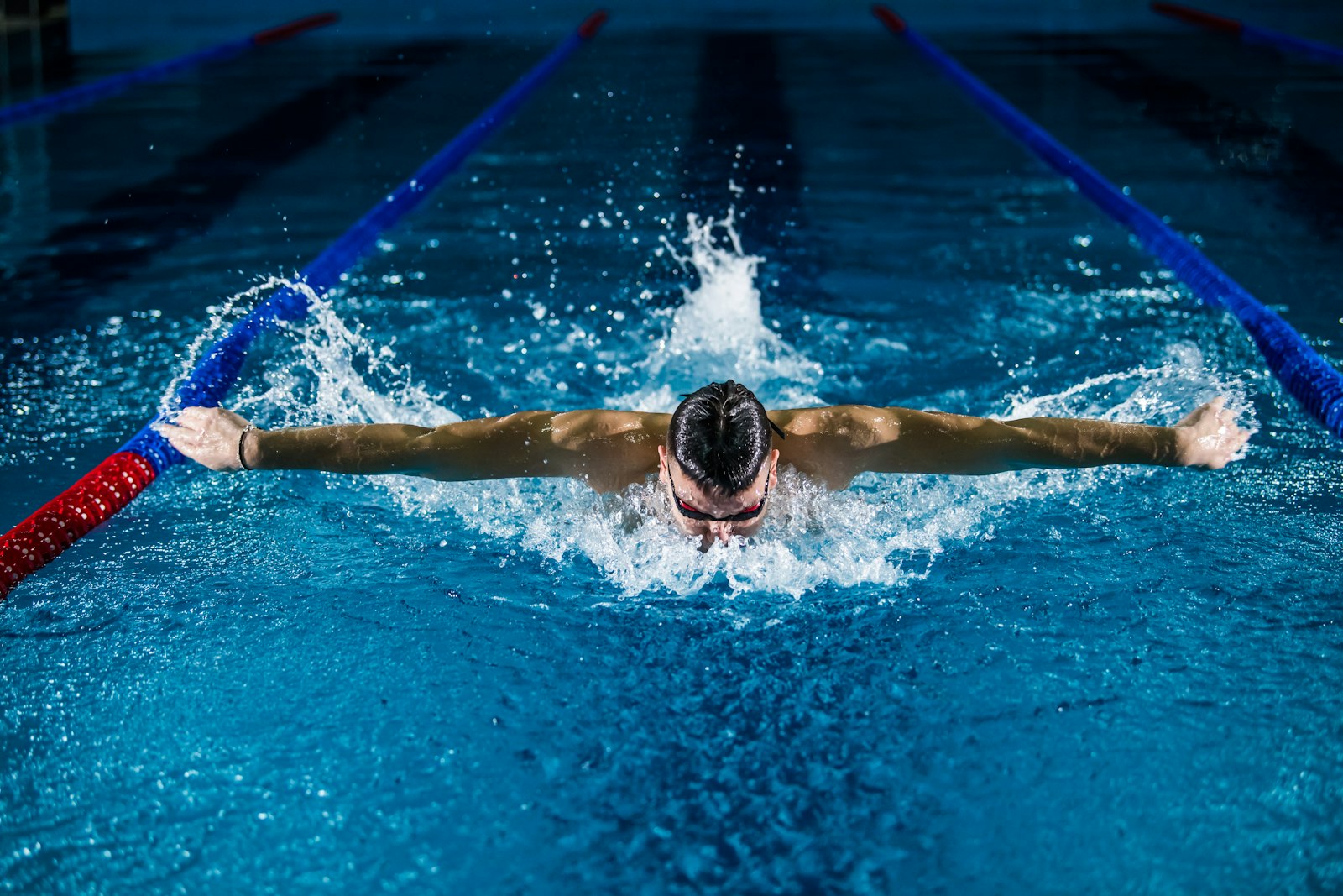 Swimmer doing butterfly stroke in a competition pool with lane ropes