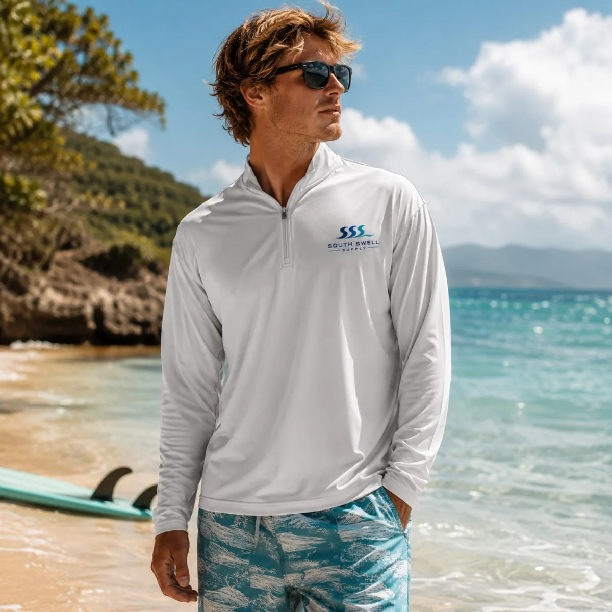 Man wearing a white long-sleeve UV sun shirt on a tropical beach with a surfboard — outdoor sun protection for surf and resort brands.
