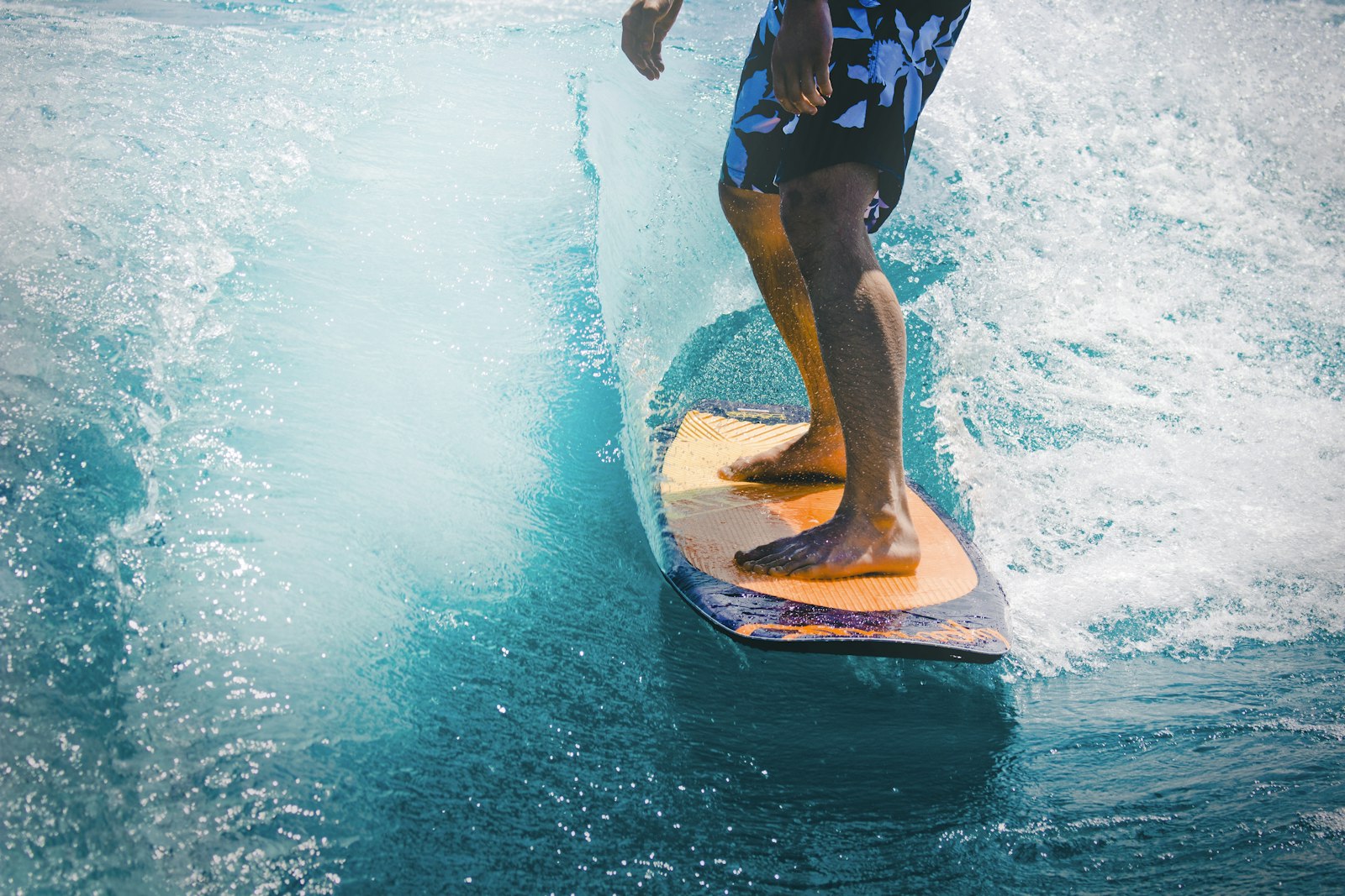 Surfer standing on a custom orange soft-top surfboard in clear water