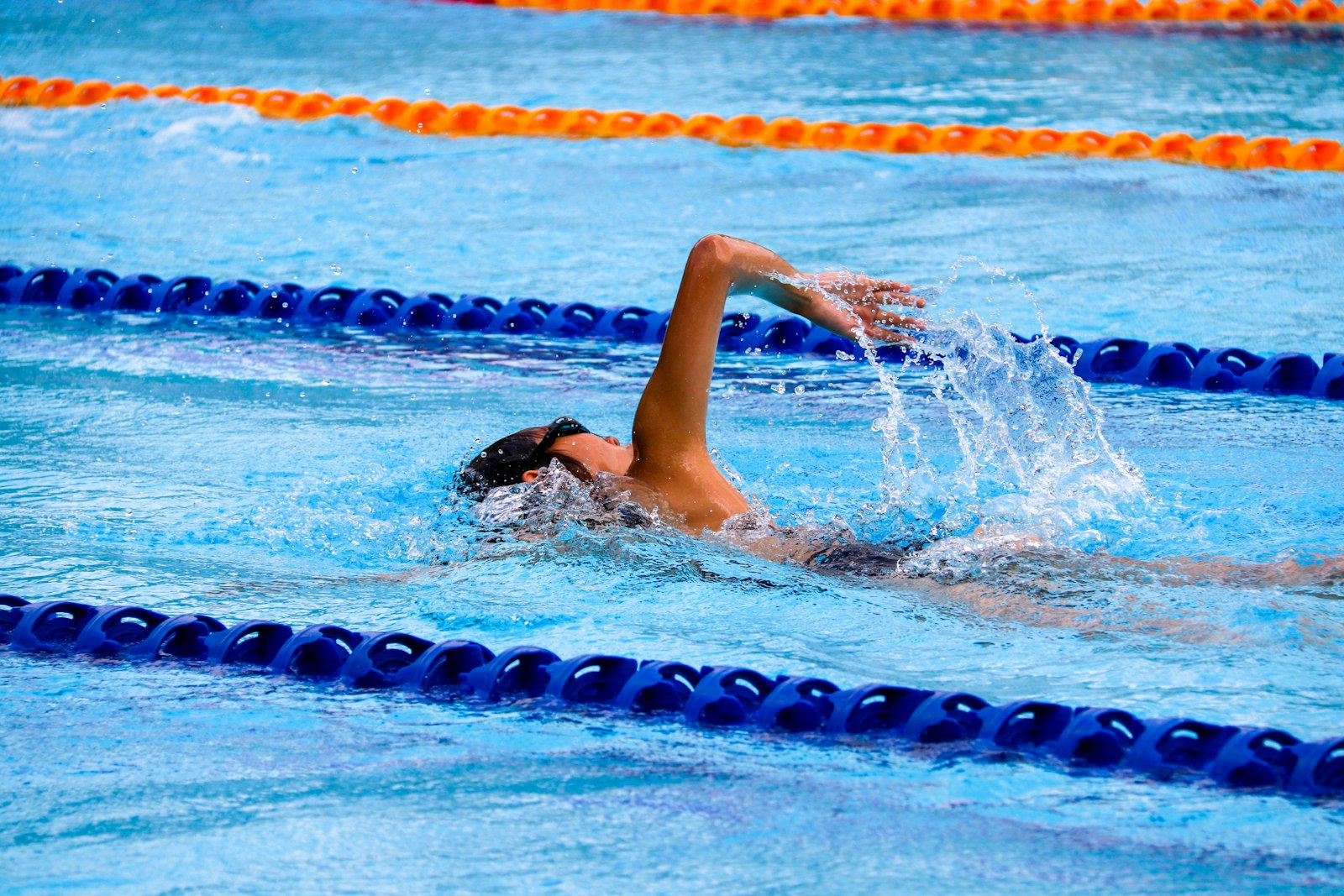 Swimmer training freestyle in an outdoor pool between lane ropes